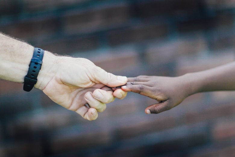 A white hand with a watch holds a smaller black hand.